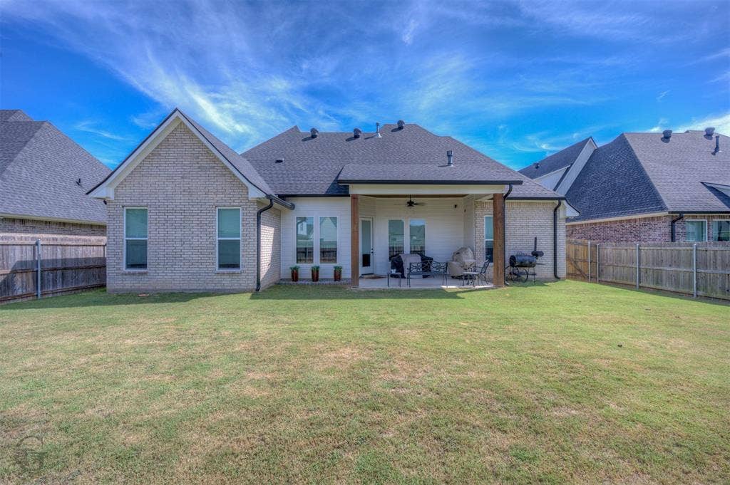 Expansive rear yard with a covered patio, exposed wood beams, and a ceiling fan