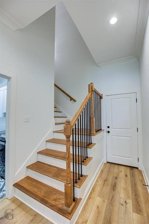 Hardwood treads with a wrought iron and wood banister, recessed lighting, crown molding, and wood-finish flooring