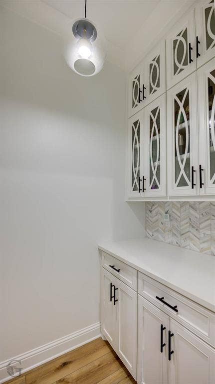 White cabinetry with decorative glass inserts, under-cabinet storage, white countertop, and herringbone tile backsplash