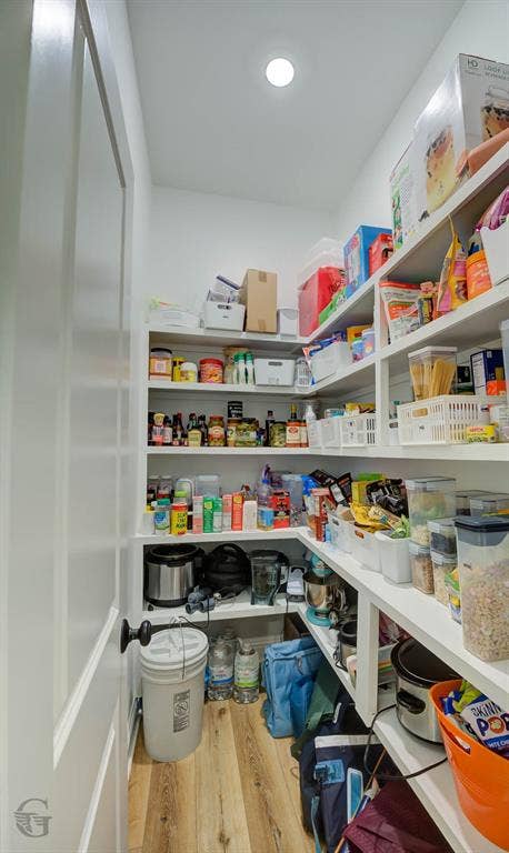 Walk-in pantry featuring extensive built-in shelving, recessed lighting, and wood-finish flooring