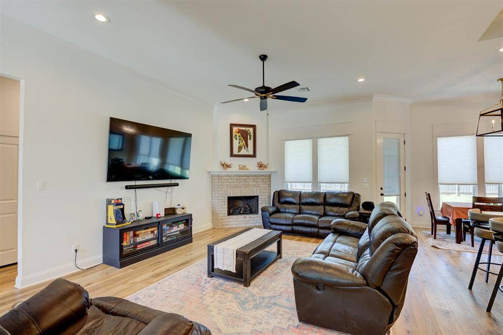 Living area featuring wood-finish flooring, a corner fireplace with brick surround, recessed lighting, and a ceiling fan