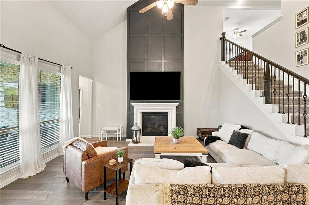Vaulted ceiling living area featuring a fireplace with a white mantel, dark paneled accent wall, wood-finish flooring, and a staircase with wrought iron balusters