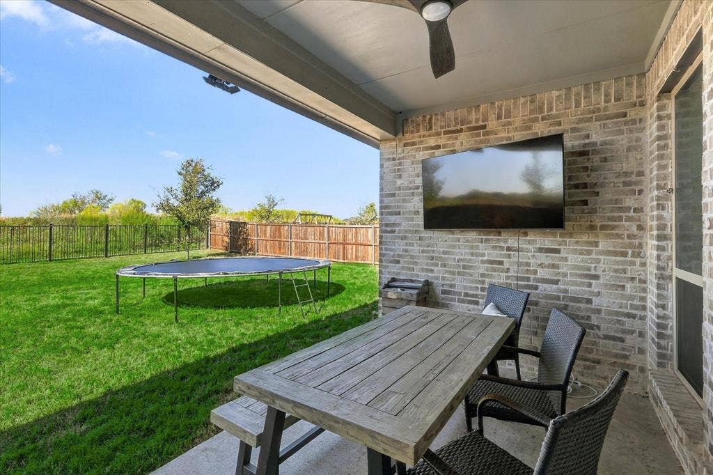 Covered patio with a mounted ceiling fan, brick accent wall, and a large television