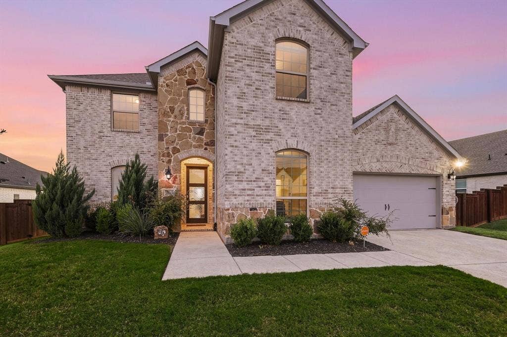 Two-story exterior featuring light brick and stone accents, an arched entry, a modern paneled front door with glass inserts, and an attached two-car garage