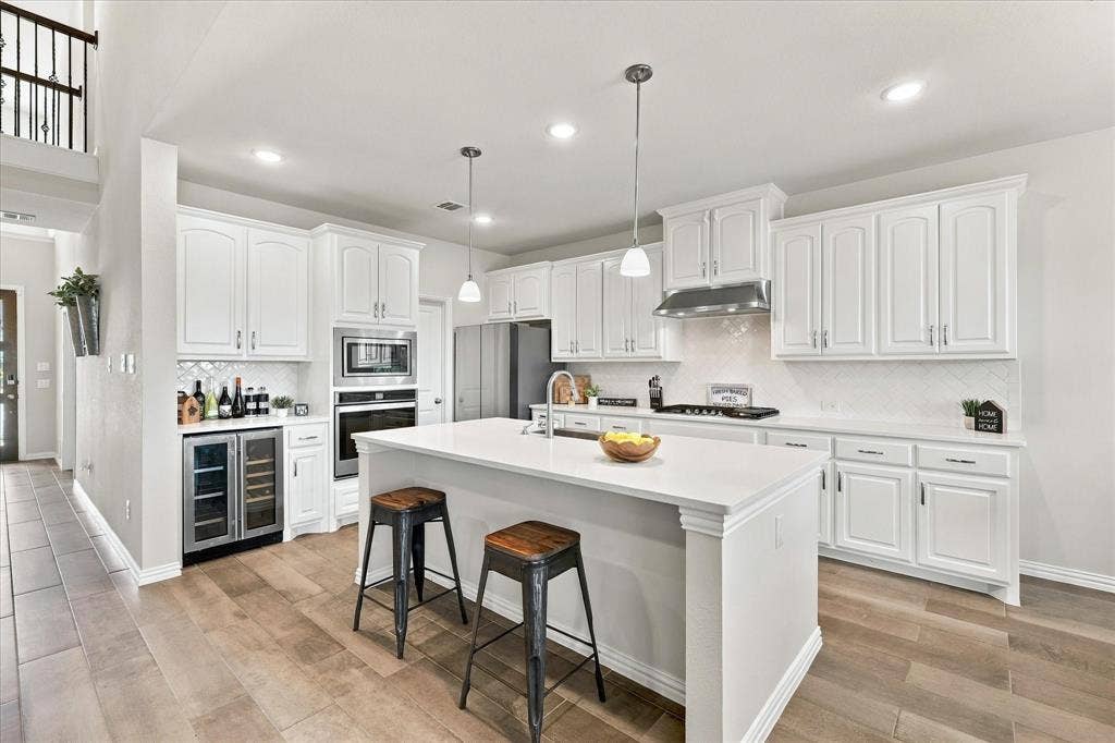 White cabinetry with stainless steel appliances, recessed lighting, and a center island with pendant lighting