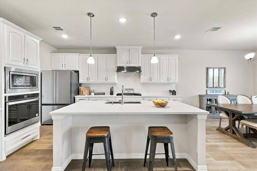 White cabinetry, stainless steel appliances, white countertop island with pendant lighting, tile backsplash, and wood-finish flooring