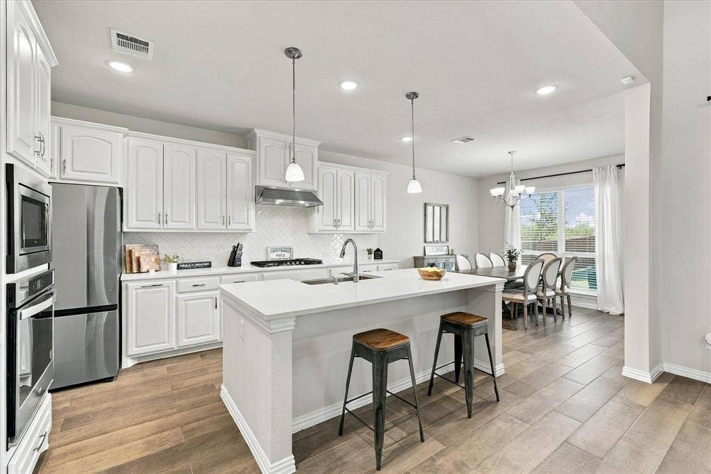 White cabinetry, stainless steel appliances, kitchen island with seating, wood-finish flooring, and a dining area with a chandelier
