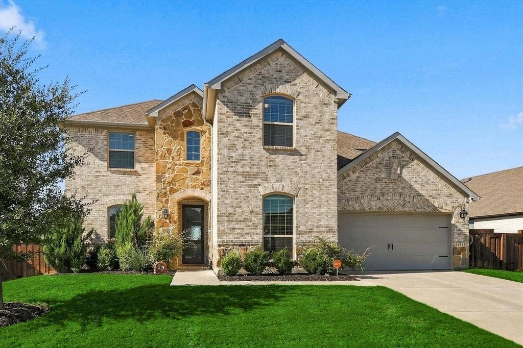 Two-story exterior with brick and stone accents, arched windows, an attached two-car garage, and a concrete driveway