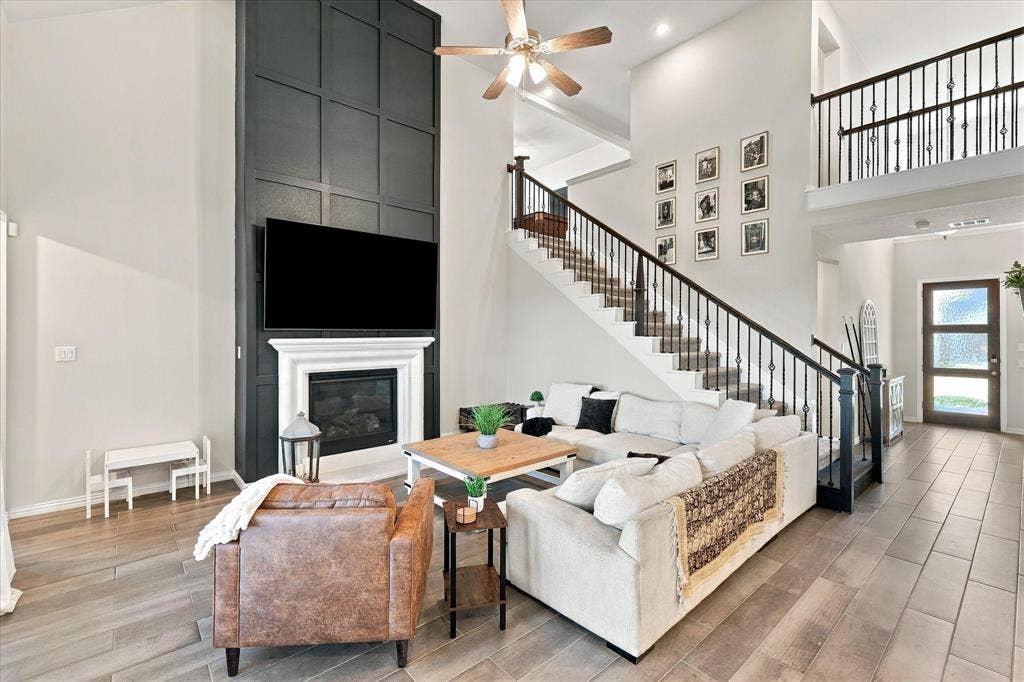 Two-story living area with high ceilings, feature wall with fireplace, recessed lighting, and a grand staircase with wrought iron balusters