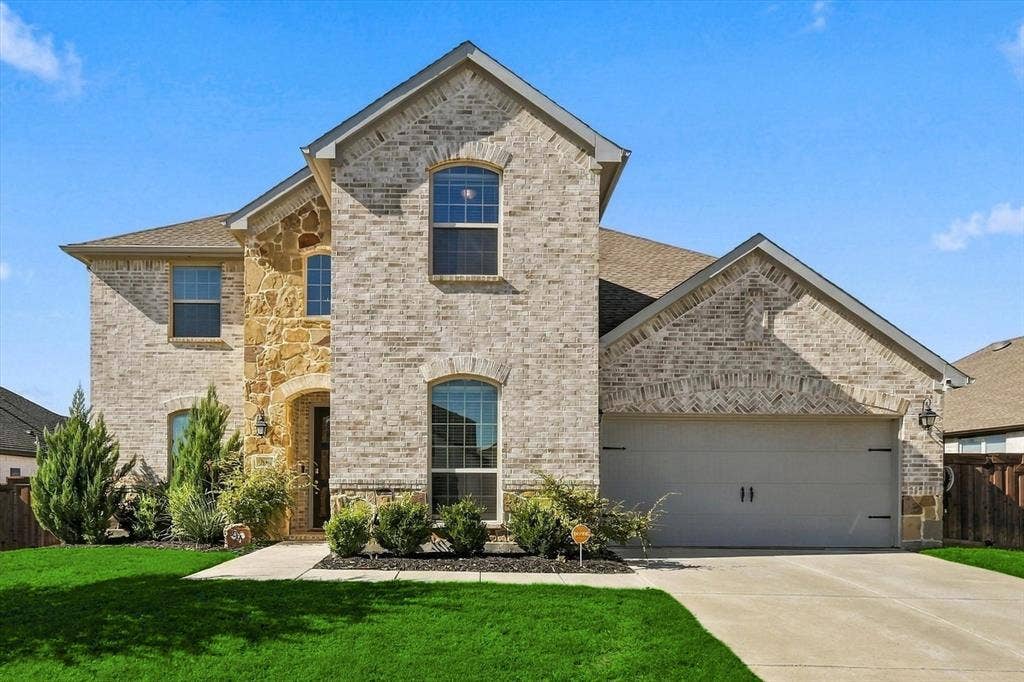 Brick and stone facade, arched entryway, gabled roofline, two-car garage, established landscaping