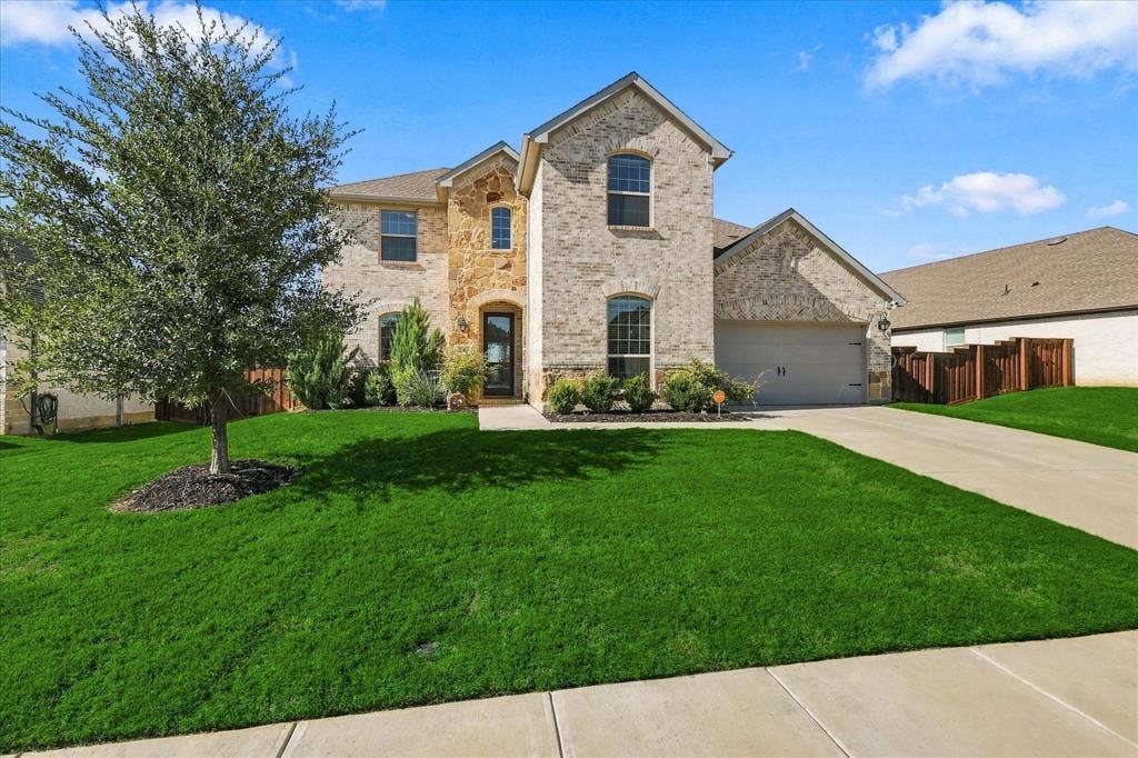 Two-story exterior with brick and stone accents, an attached two-car garage, and a concrete driveway