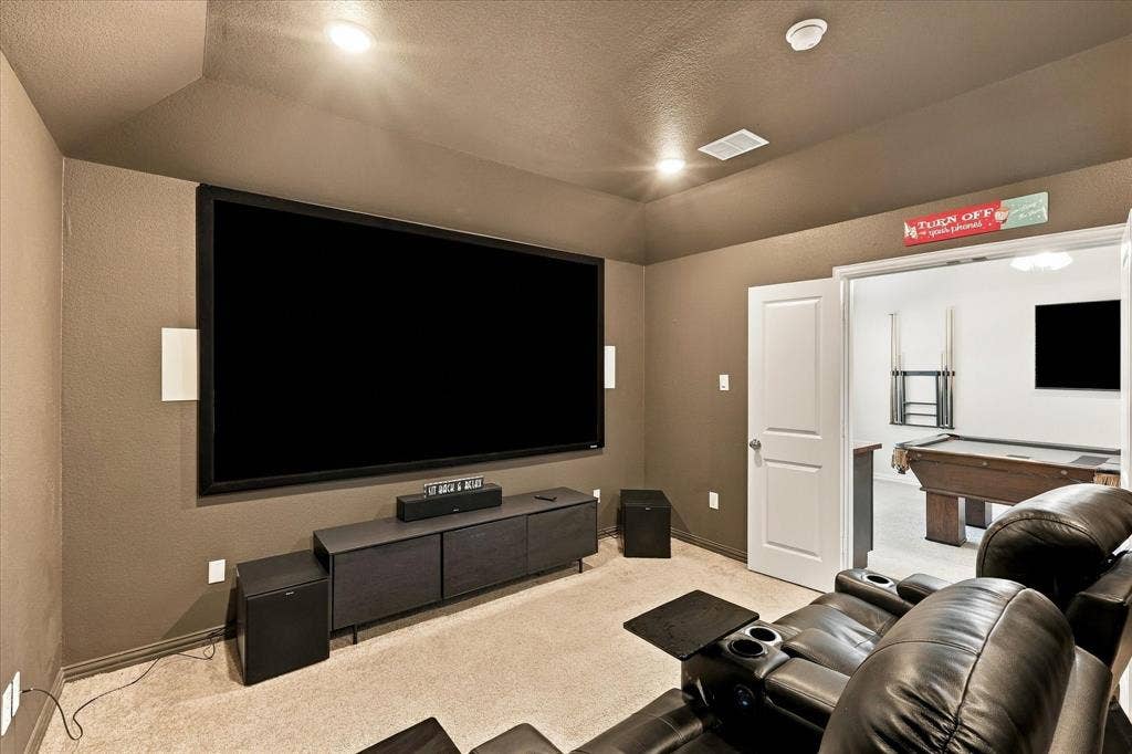 Dedicated media room featuring a large projection screen, recessed lighting, and soft carpeting