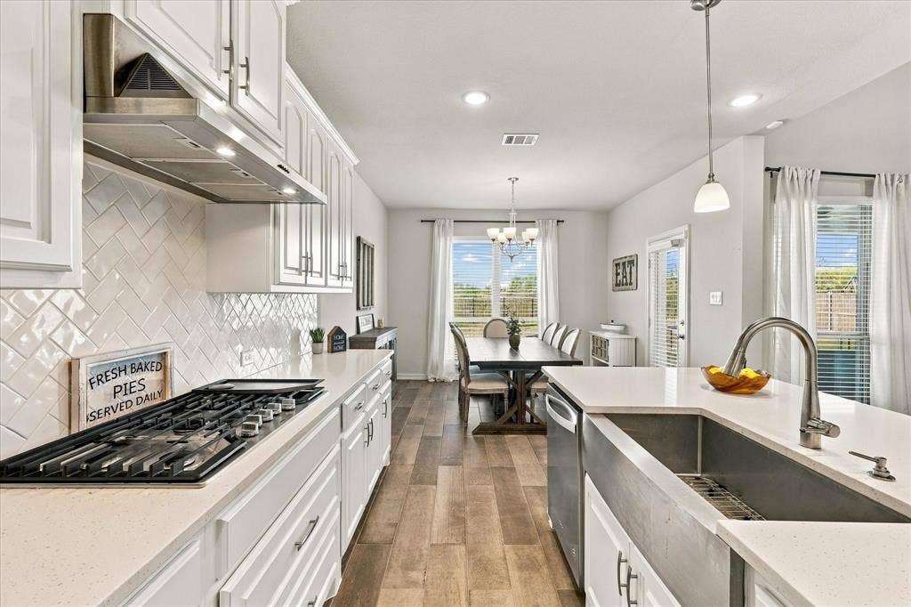 White shaker cabinetry with black hardware, herringbone tile backsplash, stainless steel range hood, built-in gas cooktop, and wood-finish flooring