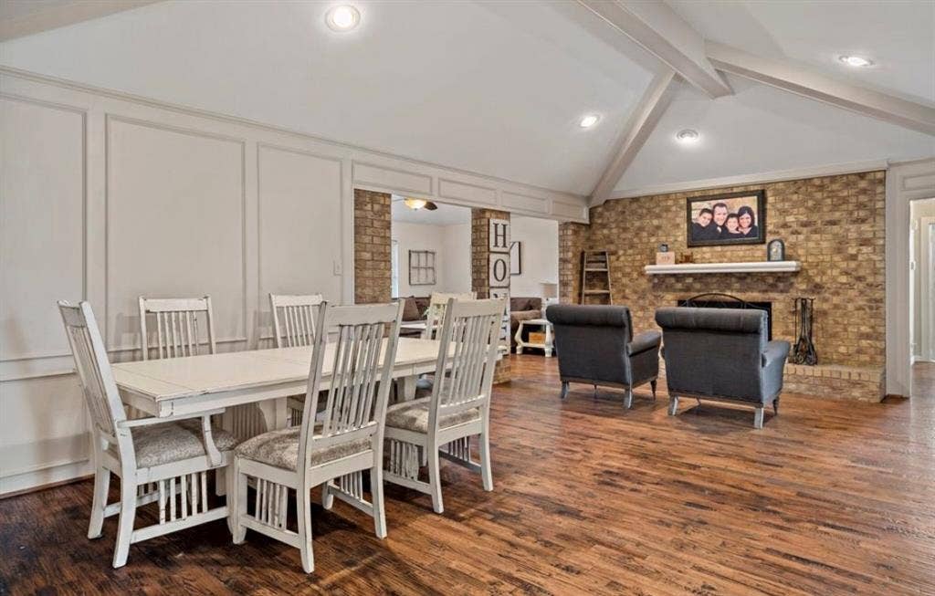 1603 Vicksburg Drive, Sachse, TX 75048 Dining area featuring vaulted ceiling with beams, a decorative wall, a brick fireplace, wood finished floors, and ornate columns