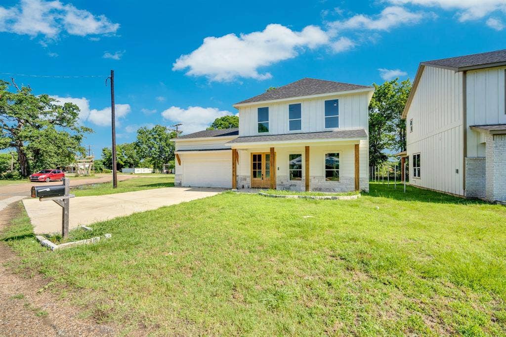 1995 Lakeview Drive, Kemp, TX 75143 Two-story property featuring white vertical siding, a covered entry with wood posts, a wood-finish front door, a concrete driveway, and a partially grassed lawn