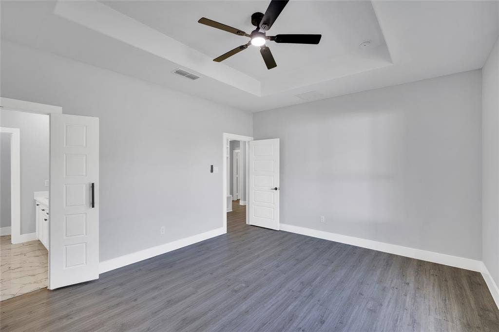 1995 Lakeview Drive, Kemp, TX 75143 Tray ceiling with a ceiling fan, wood-finish flooring, white trim, and a barn door entry to the adjacent bathroom
