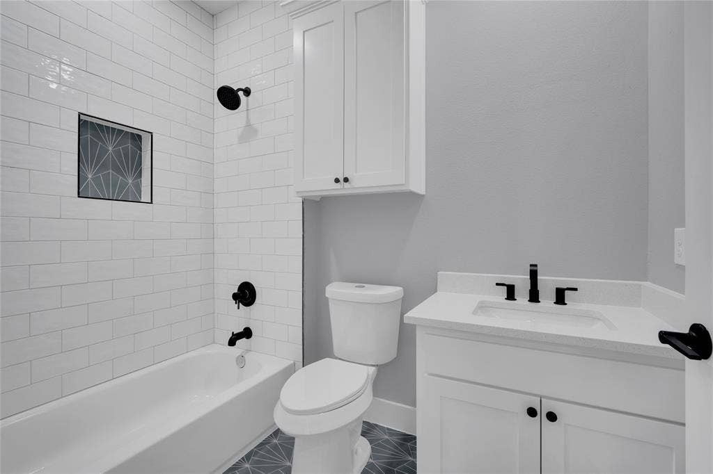 1995 Lakeview Drive, Kemp, TX 75143 White subway tile shower surround with a decorative niche, dark-finish plumbing fixtures, white vanity with an integrated sink, white upper cabinetry, and patterned floor tiling