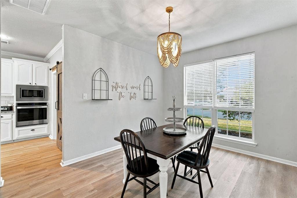 Dining area featuring wood-finish flooring, a tiered bead-embellished chandelier, dual-pane windows with horizontal blinds, and a sliding barn-style door