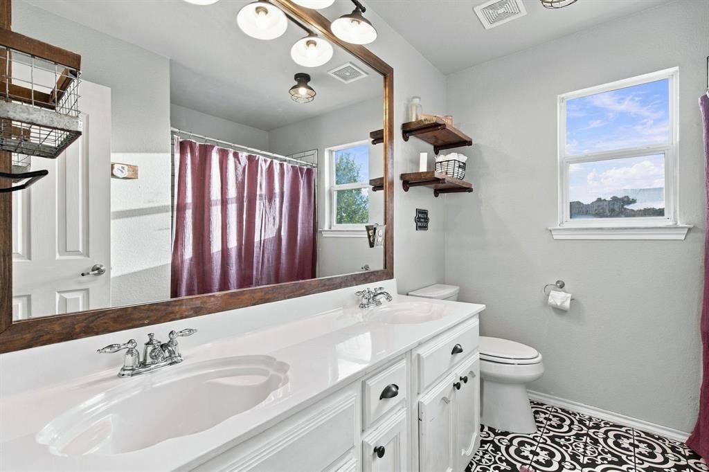 Double vanity featuring white cabinetry, a solid-surface countertop, dark hardware, and a large framed mirror