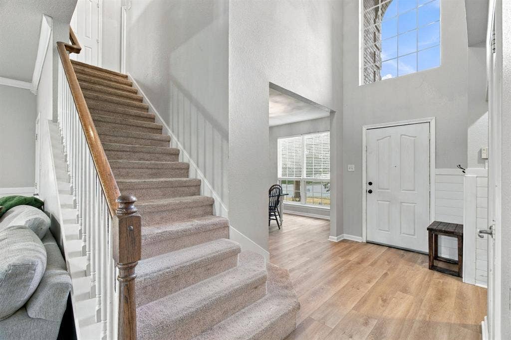 Entryway featuring high ceilings, a staircase with a wooden handrail, wood-finish flooring, and an arched window