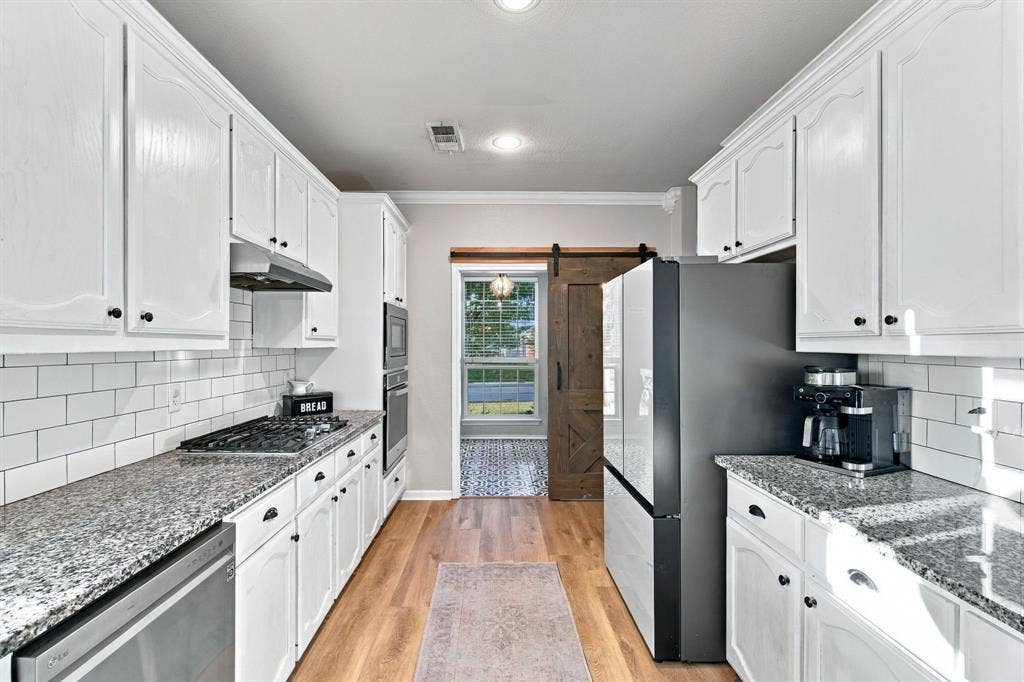Kitchen featuring white cabinetry, stone countertops, subway tile backsplash, stainless steel appliances, and wood-finish flooring