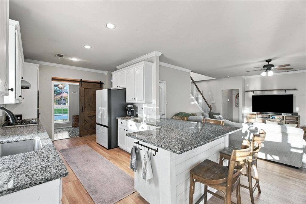 Kitchen featuring white cabinetry, stone countertops, an island with shiplap detailing, wood-finish flooring, and a sliding barn door