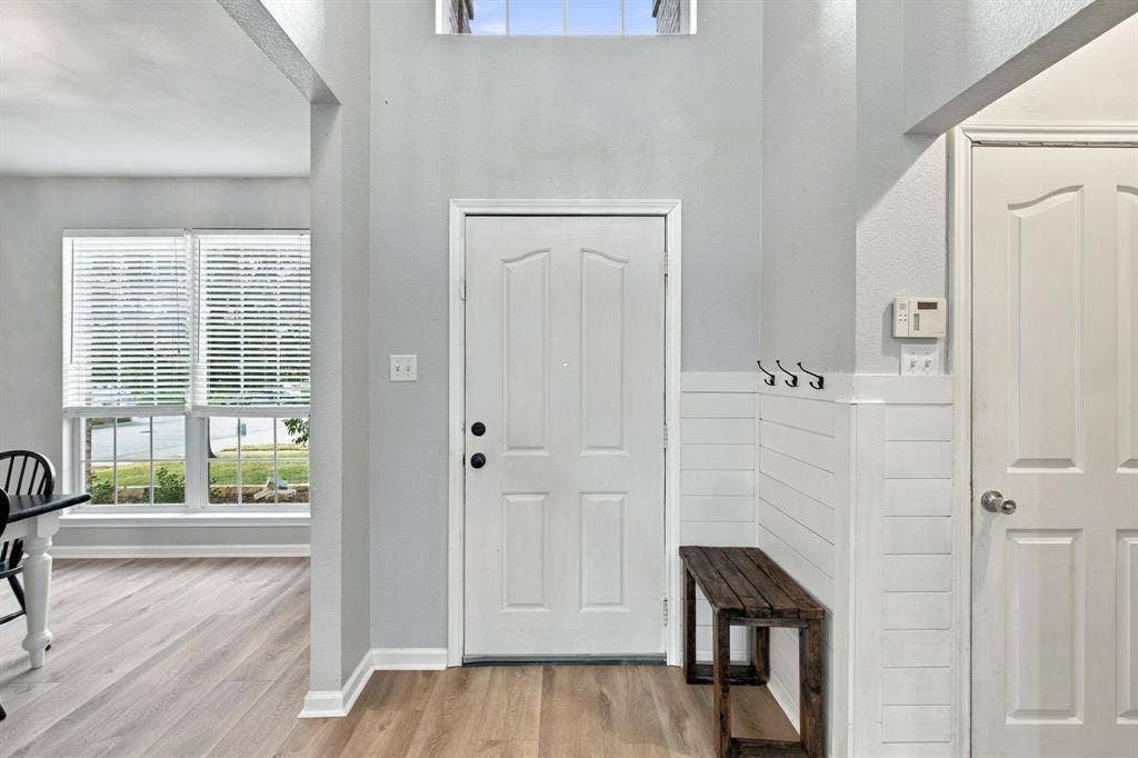 Entryway featuring high ceilings, a transom window, wood-finish flooring, and white shiplap wainscoting with integrated wall-mounted hooks