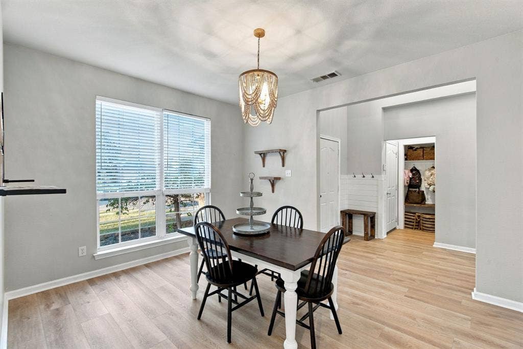 Wood-finish flooring, beaded chandelier, large windows with horizontal blinds, built-in wall shelving, and shiplap-style wall accent with coat hooks