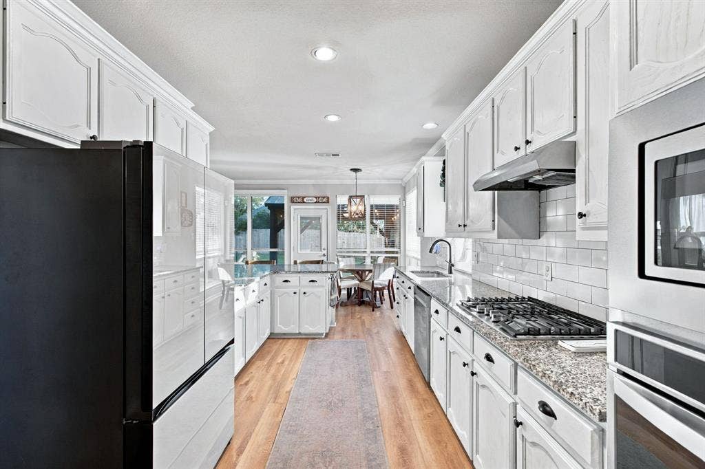 Kitchen featuring white cabinetry, stone countertops, subway tile backsplash, stainless steel appliances, and wood-finish flooring