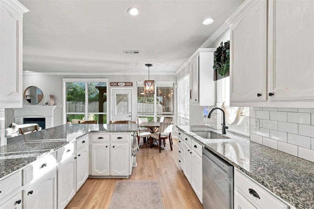 Kitchen featuring white shaker-style cabinetry, speckled stone countertops, a subway tile backsplash, stainless steel dishwasher, and wood-finish flooring