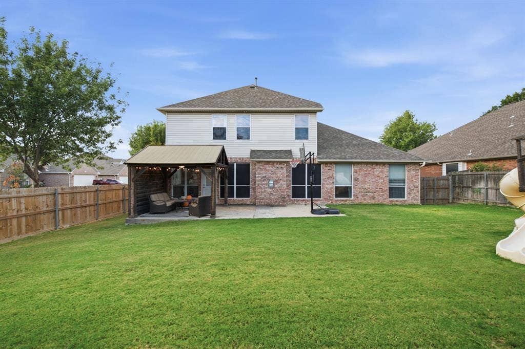 Expansive backyard featuring a manicured lawn, wood fencing, concrete patio, and a covered timber-framed structure