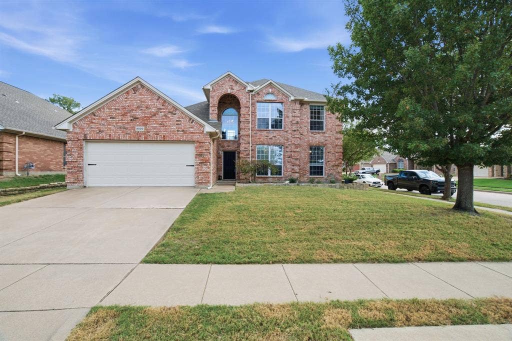 Two-story brick exterior featuring a multi-gabled roofline, an arched entryway, and an attached two-car garage