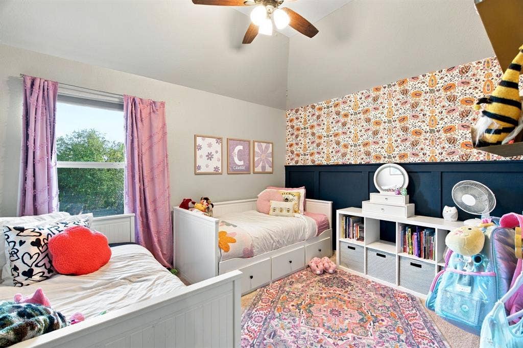 Vaulted ceiling featuring a central ceiling fan with an integrated light fixture, dark-toned wainscoting, and patterned wallpaper