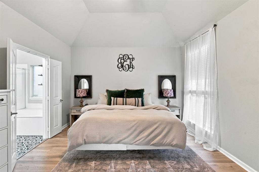 Bedroom featuring a vaulted ceiling, wood-finish flooring, and a large window