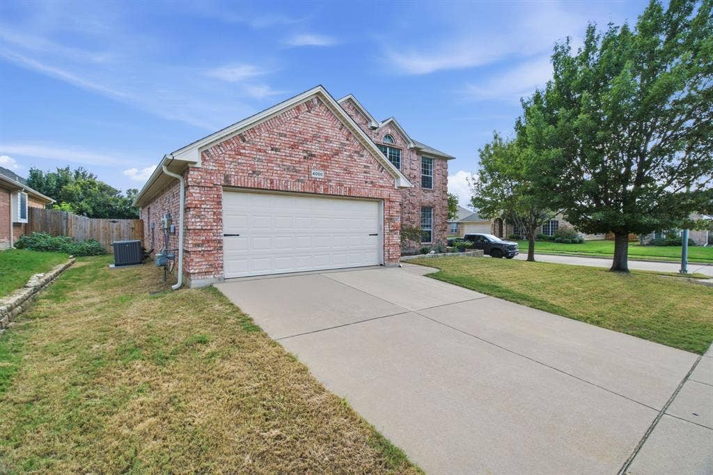 Red brick exterior featuring a multi-gabled roofline, concrete driveway, and attached two-car garage