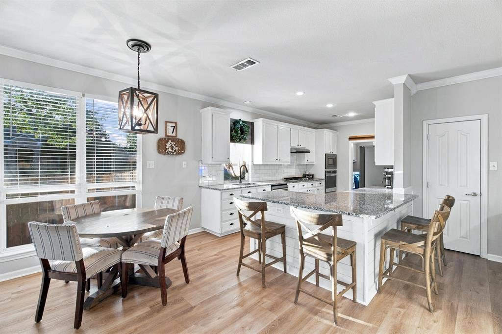 Kitchen featuring white shaker-style cabinetry, stone countertops, a center island with shiplap detailing, wood-finish flooring, and a geometric pendant light fixture