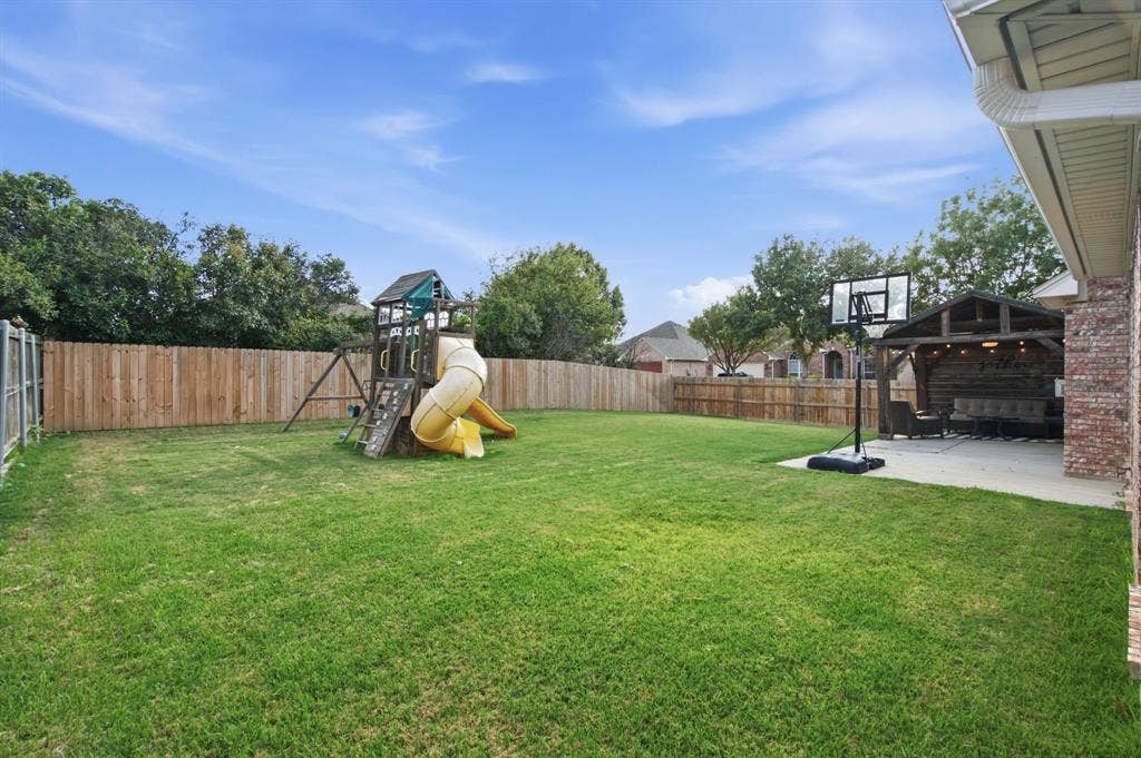 Expansive backyard featuring a manicured lawn, wood privacy fencing, a concrete patio, and a covered timber-framed structure