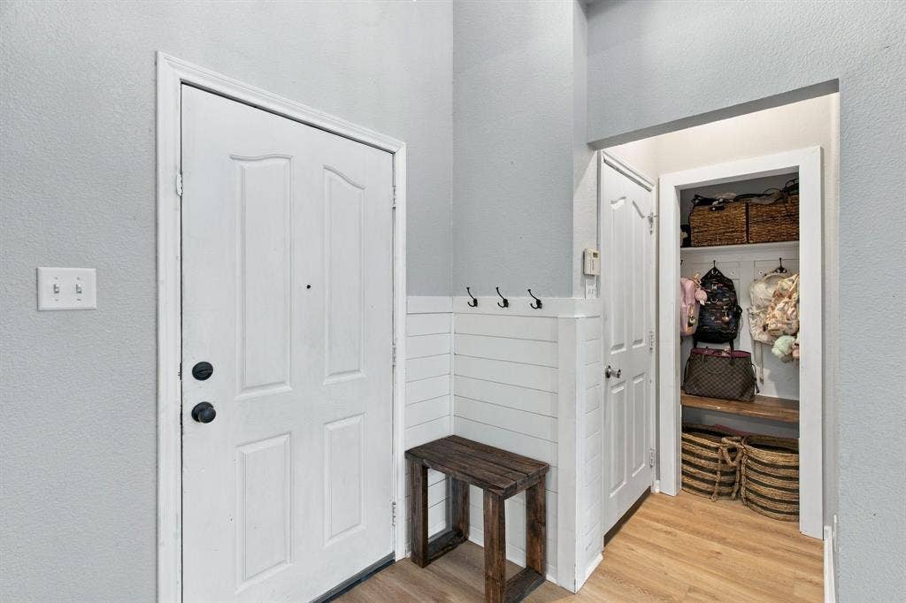 Entryway featuring white shiplap wainscoting with integrated wall hooks, wood-finish flooring, and a walk-in storage area with built-in wooden shelving