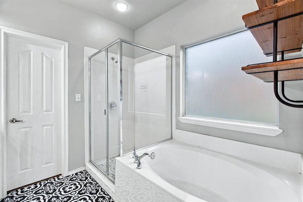 Bathroom featuring a glass-enclosed shower, a deep soaking tub, patterned floor tile, and built-in metal and wood-finish shelving