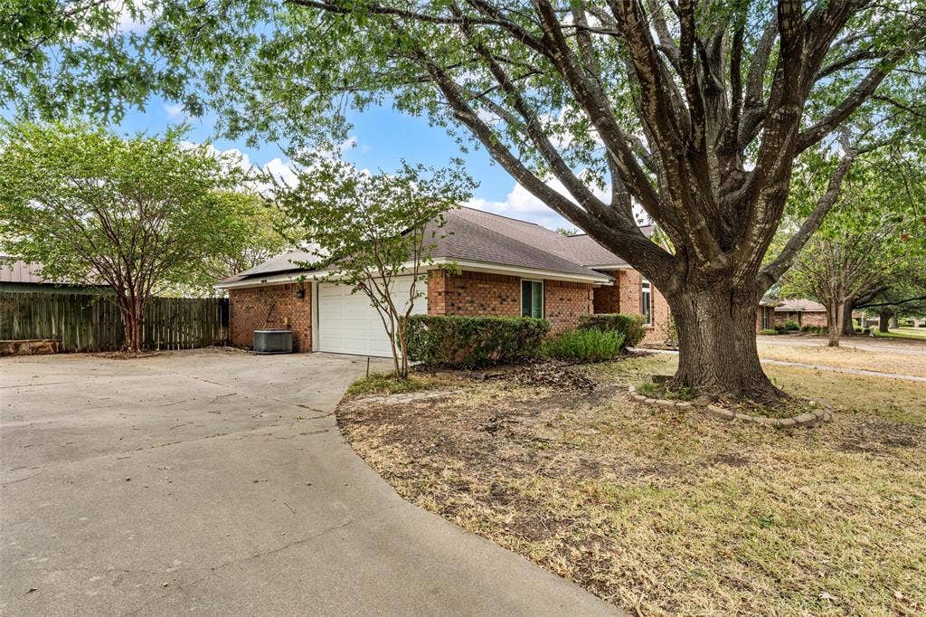 812 Regina Drive, Hewitt, TX 76643 Brick exterior with an attached garage, paved driveway, mature trees, and established landscaping