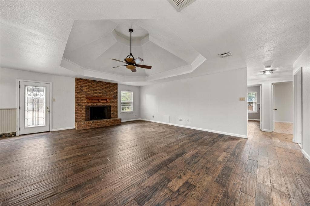 812 Regina Drive, Hewitt, TX 76643 Tray ceiling with a ceiling fan, brick-faced fireplace with a wood mantel, wood-finish flooring, and white walls