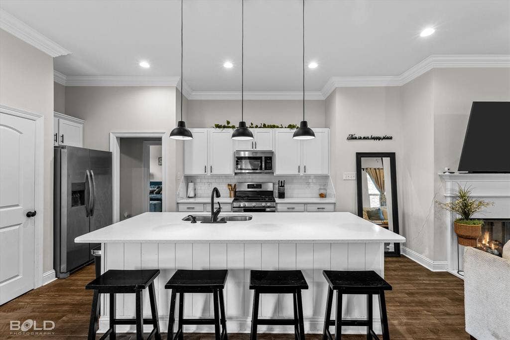 Open-concept kitchen featuring a large island with seating, stainless steel appliances, white cabinetry, and wood-finish flooring