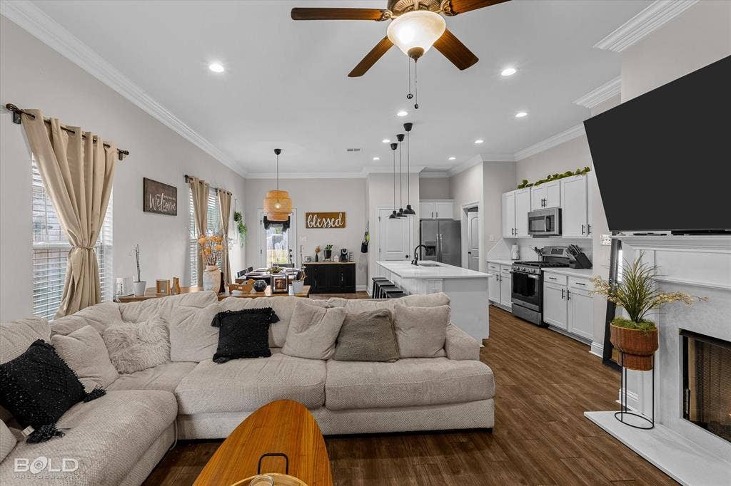 Open-concept living area featuring a fireplace, wood-finish flooring, white kitchen cabinetry, a kitchen island with seating, and recessed lighting