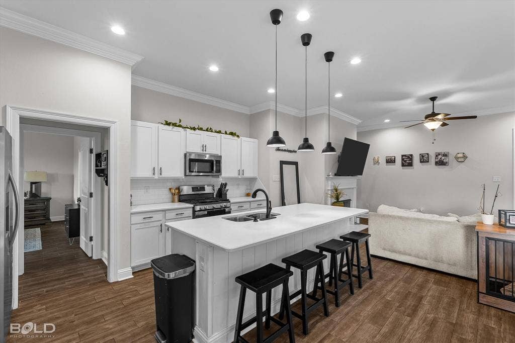 Open-concept living space with wood-finish flooring, white cabinetry, stainless steel appliances, and a kitchen island with pendant lighting