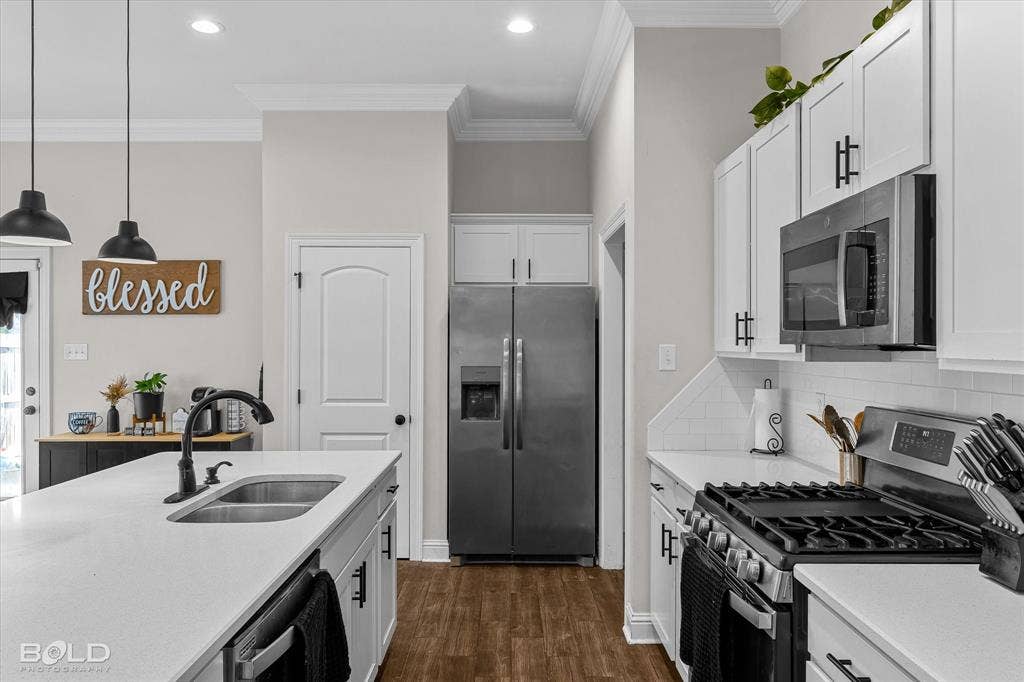 Kitchen featuring an island with an undermount double-basin sink, white cabinetry with black hardware, stainless steel appliances, and wood-finish flooring