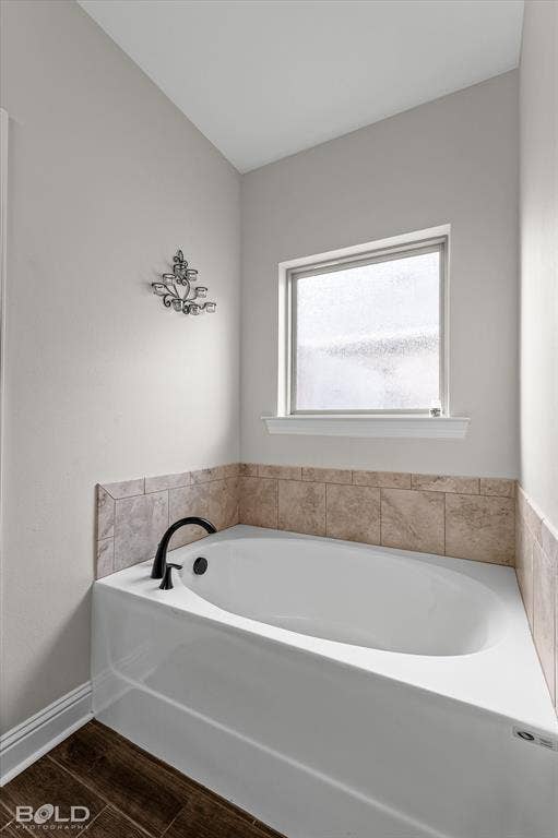 Built-in soaking tub with matte black fixtures, tile surround, and wood-finish flooring