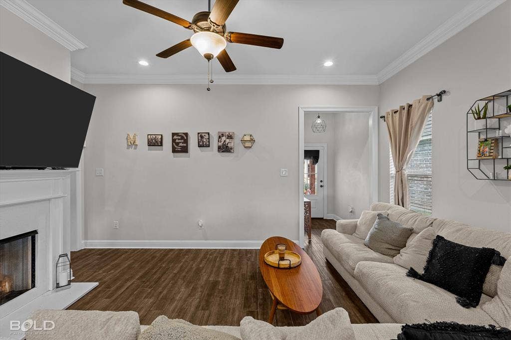 Wood-finish flooring throughout, crown molding, ceiling fan with integrated lighting, recessed lighting, and a white mantelpiece