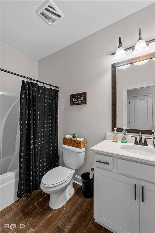 Wood-finish tile flooring, white vanity with integrated sink, dark bronze hardware, white bathtub with shower, and vanity lighting