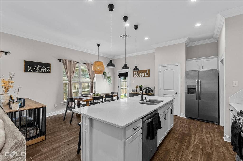 Spacious kitchen featuring an expansive island with an undermount sink, stainless steel appliances, wood-finish flooring, and crown molding