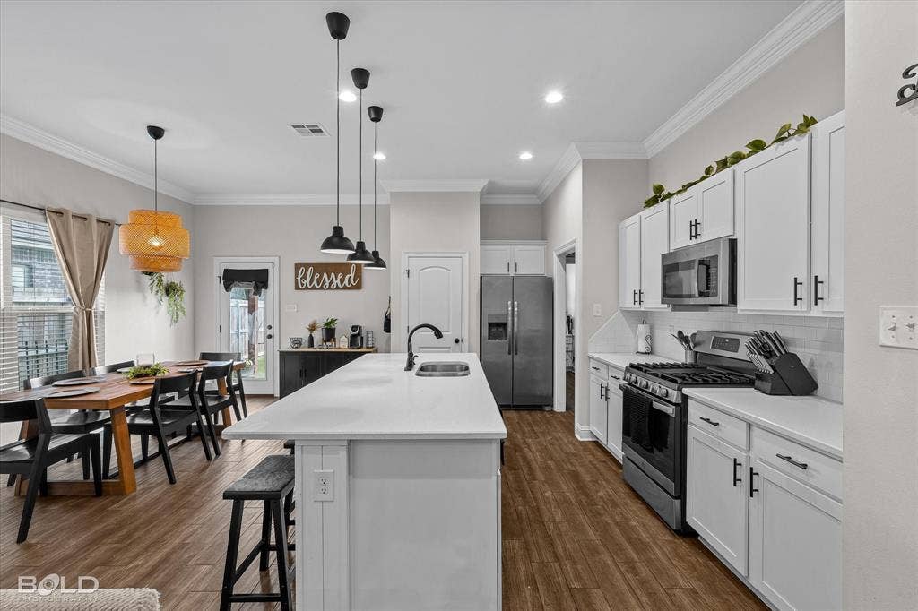 Open-concept kitchen and dining area featuring wood-finish flooring, white cabinetry, a kitchen island with seating, stainless steel appliances, and recessed lighting
